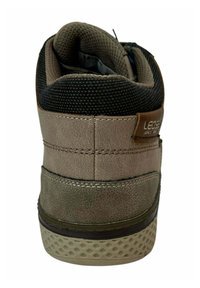 Zapato alto de piel marrón con un cuello de malla negra texturizada, costuras reforzadas y una suela de goma con patrón. Muestra la vista trasera con detalles del logo.