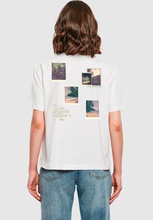 T-shirt en coton blanc avec une coupe oversize, mettant en avant plusieurs images graphiques de palmiers et d'un coucher de soleil, ainsi que le texte "Puerto Rico" en jaune.