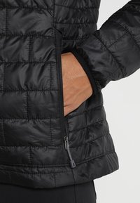 Svart isolerad jacka med ett quiltat mönster, som har en dragkedjeficka på sidan och elastisk trim längs ärmsluten och nederkanten.