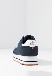 Námořnické modré tenisky s texturovaným svrškem, bílými akcenty, logem na patě a gumovou podrážkou. Mají polstrovaný límec pro pohodlí.