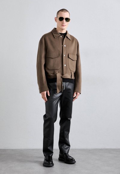 Brown wool blend jacket with large front pockets, tied waist, and button closure, paired with glossy black leather pants and black shoes.