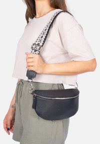 Schwarze Leder-Umhängetasche mit strukturierten Oberflächen, silbernem Reißverschluss und verstellbarem, gemustertem Trageriemen. Kompakte, abgerundete Form mit metalischen Hardware-Details.