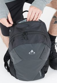 Czarny plecak z teksturowaną powierzchnią, podwójnymi suwakami i logo. Posiada siateczkowe boczne kieszenie oraz wygodne, wyściełane szelki. Główna komora jest otwarta.