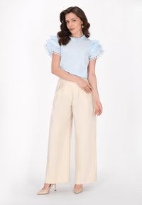 Camicia azzurro chiaro con maniche a volant rifinite in pizzo, abbinata a pantaloni beige a gamba larga e scarpe con tacco beige.