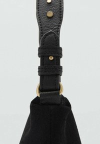 Crni remen za torbu od brušene kože s glatkim crnim kožnim detaljima i zlatnim ukrasima s kopčom i ukrasnim zakovicama.