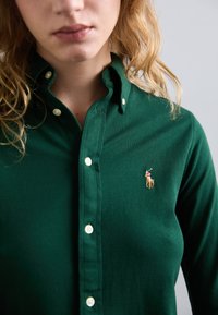 Cămașă verde cu nasturi, confecționată dintr-un material texturat, având un mic logo de jucător de polo brodat și nasturi albi.