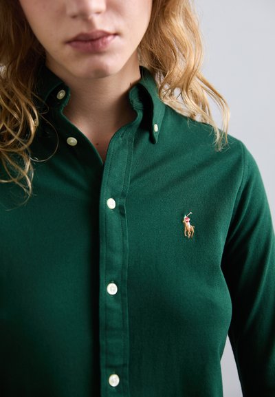 Grønn skjorte med knapper laget av teksturert stoff, med en liten brodert polo-spiller-logo og hvite knapper.