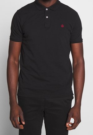 Polo noir en coton, avec un col classique, une patte de boutonnage à trois boutons et un petit emblème rouge sur le côté gauche de la poitrine.
