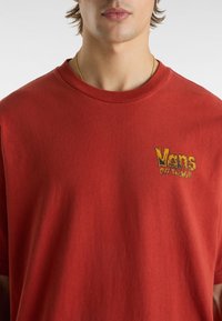 Rød bomulds T-shirt med rund hals, prydet med det gule "Vans Off The Wall" logo broderet på venstre bryst. Blød tekstur, afslappet pasform.