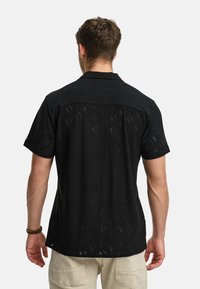 Black short-sleeve shirt featuring a textured, perforated design with a geometric pattern and a classic collar. Lightweight fabric.