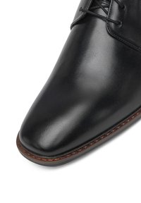 Melns ādas kleitu kurpes ar norādītu purngalu, gludu tekstūru un kontrastējošu brūnu dūrienu gar zoli, lai pievienotu sīkākas detaļas.