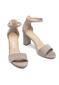 Beżowe zamszowe sandały na obcasie z szerokim paskiem na przodzie, paskiem na kostkę z klamrą oraz masywnym obcasem. Gładka tekstura i minimalistyczny design.