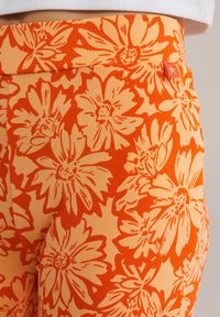 Cvečne legice z oranžno in kremno barvo velike marjetice, narejene iz rebrastega raztegljivega materiala z širokim pasom.