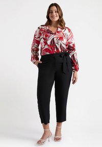 Blusa floreale con motivi di foglie rosse e verdi, abbinata a pantaloni neri cropped con vita legata. Il modello indossa tacchi bianchi con cinturini.
