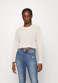 Lys beige cropped sweater med tekstureret strikmønster og lange ærmer, parret med mid-rise blå jeans med slidte detaljer.