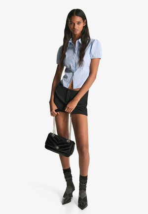 Blauw-wit gestreepte shirt met korte mouwen, zwarte shorts, een zwart gewatteerde tas en schoenen met spitse neuzen, met textuur zwarte sokken.