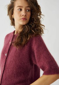 Vinklædt strikket cardigan med korte ærmer, der har en blød, fuzzy tekstur og to knapper foran.