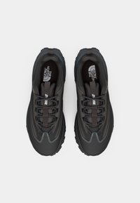 Zapatillas deportivas negras con una superficie texturizada, que cuentan con un diseño de cordones, puntera reforzada y un logotipo prominente en la lengüeta.