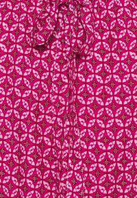 Tessuto rosa a motivo con design circolari e floreali, con accenti bianchi e piccoli punti. Il materiale è leggero e texture.