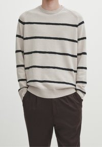 Beige gestreifter Pullover aus weichem Material mit schwarzen horizontalen Streifen, Rundhalsausschnitt, gerippten Bündchen und Saum. Kombiniert mit dunklen Hosen.