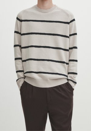 Beige gestreifter Pullover aus weichem Material mit schwarzen horizontalen Streifen, Rundhalsausschnitt, gerippten Bündchen und Saum. Kombiniert mit dunklen Hosen.