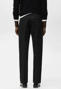 Schwarze, maßgeschneiderte Hose mit seitlichen und hinteren Taschen, geradem Bein und glatter Textur. Kombiniert mit einem schwarzen Pullover.