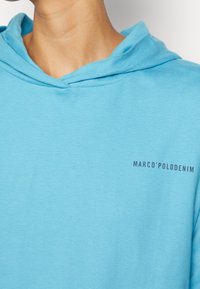 Hoodie bleu clair en coton doux, avec une coupe décontractée, une capuche avec cordon de serrage et un petit logo noir sur le devant.