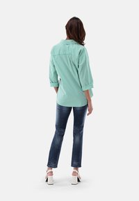 Green and white striped shirt, collared, with three-quarter sleeves, paired with blue denim jeans and white block-heeled sandals.