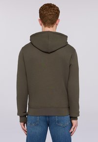 Oliwkowa bluza z kapturem ze sznurkiem, z prążkowanymi mankietami i dołem, wykonana z teksturowanej tkaniny. Noszona z niebieskimi dżinsami. Widok z tyłu.