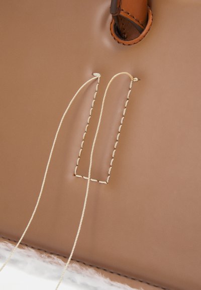 Torbica iz svetlega usnja z pravokotnim šivanim detajlom v kremni barvi, ki prikazuje gladko teksturo in subtilne oblikovne elemente.