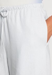 Lichtgrijze linnen broek met elastische tailleband en trekkoord, hand casual geplaatst in de rechterzak.