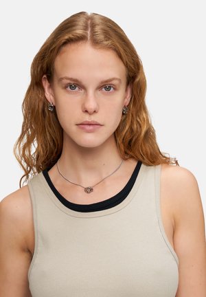 Silberne Schmuckstücke mit miteinander verbundenen kreisförmigen Designs, getragen mit einem beigen Tanktop. Merkmale sind eine glatte Textur und dezenter Glanz.