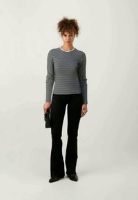 Camisola de mangas longas riscada em azul-marinho e branco, combinada com calças pretas à boca de sino. Simplicidade no design com um decote redondo; modelo segura uma pequena bolsa.