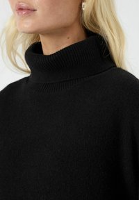 Czarny sweter z golfem o karbowanym dekolcie. Miękka tekstura, luźny krój i minimalistyczny design, bez dodatkowych wzorów czy zdobień.