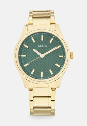 Montre en métal doré avec un cadran texturé vert, des marqueurs inclinés et une lunette lisse. Elle est dotée d'un bracelet à maillons et d'une couronne sur le côté.