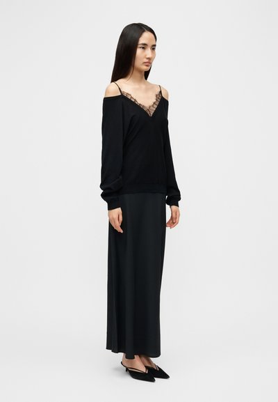 Haut noir à épaules dénudées avec bordure en dentelle, assorti d'une longue jupe noire et de chaussures noires pointues. Tissu lisse, coupe décontractée.