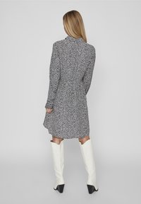 Abito floreale bianco e nero con vita cintrata, maniche lunghe e lunghezza sopra il ginocchio, abbinato a stivali bianchi al ginocchio.