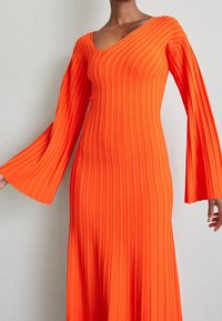 Robe orange côtelée avec un décolleté en V et des manches évasées, présentant des rayures verticales et une silhouette ajustée qui s'élargit à l'ourlet.