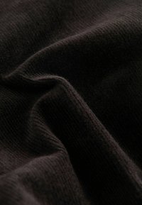 Tissu tricoté noir doux avec une texture fine et un motif côtelé visible, montrant des plis et des ombres délicates.