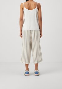 Top bianco in camisole con spalline sottili, pantaloni ampi a righe beige e scarpe da corsa con dettagli blu, su uno sfondo neutro.