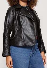 Svart lädermotorcykeljacka med dragkedja fram och sidofickor, med en kortad design och mjuk textur. I kombination med blå jeans.