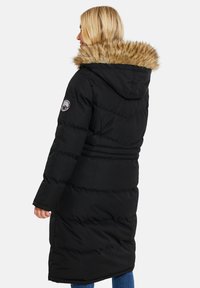 Sort pufferjakke med pelsforet hætte, lange ærmer og snøret talje. Har quiltet tekstur og et logo-patch på armen.