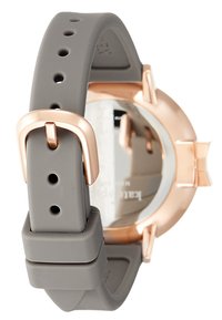 Cinturino in silicone grigio con più fori e dettagli in metallo color oro rosa. Cassa dell'orologio liscia e arrotondata sul retro, con un quadrante riflettente.