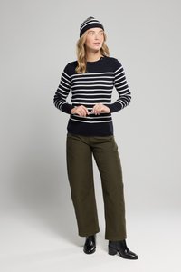 Niebiesko-białe paskowane sweter wykonany na drutach połączony z oliwkowymi szerokimi spodniami, noszony z czarnymi botkami i pasującą paskowaną czapką.