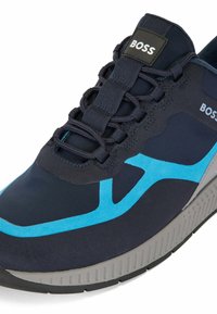 Chaussure de sport bleu marine et bleue présentant une surface texturée, un talon renforcé et une tige en mesh respirant. Logo sur la languette et lignes de design distinctives.