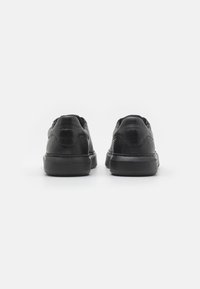 Czarne skórzane trampki z teksturowanym wykończeniem, zaokrąglonym noskiem i czarną gumową podeszwą. Oferują minimalne detale przeszycia oraz płaski design sznurówek.