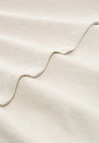 Beżowa tkanina o gładkiej teksturze, prezentująca miękkie fałdy oraz subtelny prążkowany wzór wzdłuż krawędzi.