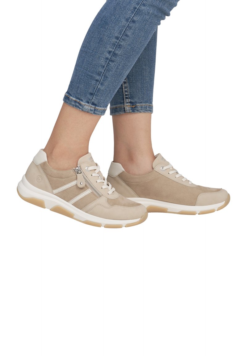 Baskets beiges avec un mélange de daim et de matériau lisse, dotées d'une fermeture éclair sur le côté, d'accents blancs et d'une semelle en caoutchouc.