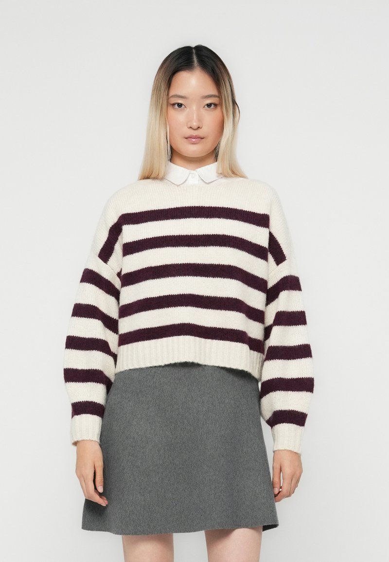 Pull en crochet avec des rayures horizontales bordeaux et crème, à manches larges et ourlet côtelé, associé à une jupe évasée grise.