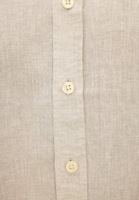 Beige Leinenhemd Vorderseite mit durchgehendem Knopfleisten, die drei helle Cremefarbene, vierlochige Knöpfe zeigt, Nahaufnahme des Stofftextures.